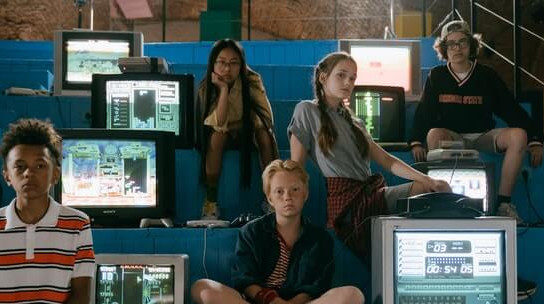 a group of kids in a hall sitting next to computers